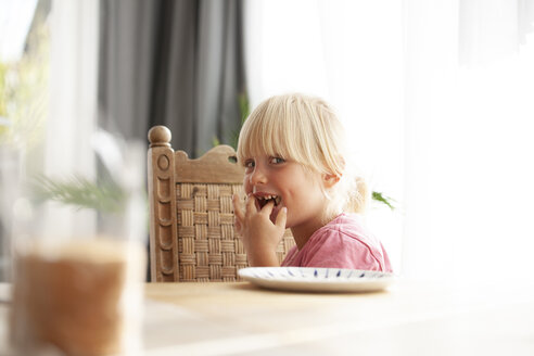 Portrait of tricksy little girl sitting at dining table eating - GAF00109