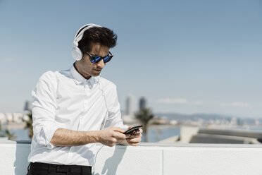 Porträt eines Geschäftsmannes, der mit Kopfhörern und Smartphone auf der Dachterrasse Musik hört - AFVF02667