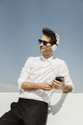 Porträt eines Geschäftsmannes, der mit Kopfhörern und Smartphone auf der Dachterrasse Musik hört - AFVF02669