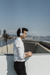 Profil eines Geschäftsmannes, der auf einer Dachterrasse mit Kopfhörern und Smartphone Musik hört - AFVF02675