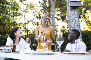 Freunde bei einem sommerlichen Abendessen im Garten öffnen eine Flasche Wein - ABZF02269