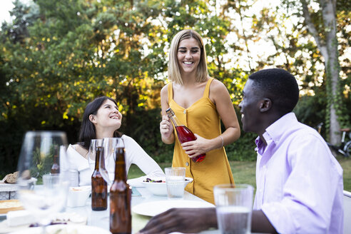 Friends at a summer dinner in the garden opening bottle of wine - ABZF02270