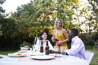 Freunde bei einem sommerlichen Abendessen im Garten öffnen eine Flasche Wein - ABZF02271