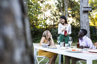 Freunde bei einem sommerlichen Abendessen im Garten öffnen eine Flasche Wein - ABZF02272