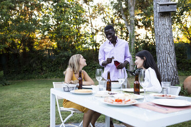 Freunde bei einem sommerlichen Abendessen im Garten öffnen eine Flasche Wein - ABZF02273