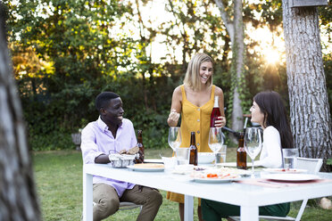 Freunde bei einem sommerlichen Abendessen im Garten öffnen eine Flasche Wein - ABZF02274