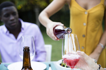 Host pouring wine into glasses at a summer dinner in the garden - ABZF02275