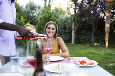 Gastgeber gießt bei einem Sommeressen im Garten Wein in Gläser ein - ABZF02277