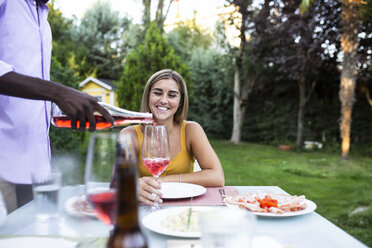 Host pouring wine into glasses at a summer dinner in the garden - ABZF02277