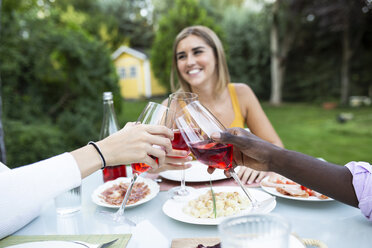 Friends toasting with wine ata summer dinner in the garden - ABZF02281