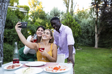 Freunde haben Spaß bei einem sommerlichen Abendessen im Garten und machen Selfies - ABZF02285