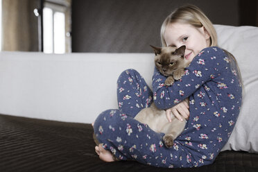 Porträt eines lächelnden kleinen Mädchens, das einen Pyjama mit Blumenmuster trägt und eine Katze hält - EYAF00073