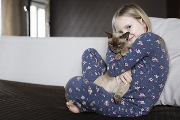 Portrait of smiling little girl wearing pyjama with floral design holding cat - EYAF00073