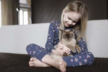 Lächelndes kleines Mädchen im Pyjama mit Blumenmuster zu Hause, das eine Katze hält - EYAF00074