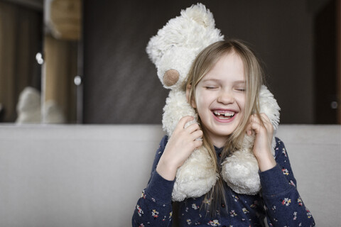 Porträt eines lachenden kleinen Mädchens mit Zahnlücke, das einen weißen Teddybären hält, lizenzfreies Stockfoto