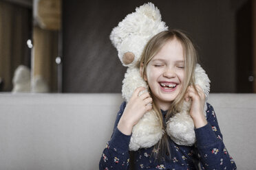 Porträt eines lachenden kleinen Mädchens mit Zahnlücke, das einen weißen Teddybären hält - EYAF00078