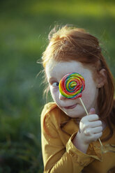 Grimacing girl covering her eye with a lollipop - GAF00114