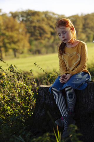 Rothaariges Mädchen sitzt auf einem Baumstumpf, lizenzfreies Stockfoto