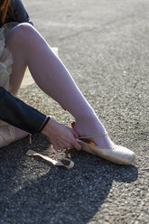 Nahaufnahme einer Frau, die sich hinsetzt und Ballettschuhe anzieht - GIOF05952