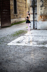 Italien, Verona, Frau im Ballettkleid mit Handy und Kopfhörer vor einem alten Gebäude stehend - GIOF05957