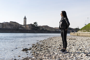 Italy, Verona, smiling young woman standing at the riverside - GIOF05959
