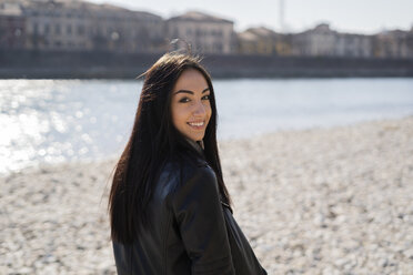 Italy, Verona, portrait of smiling young woman at the riverside - GIOF05960