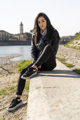 Italien, Verona, Porträt einer jungen Frau am Flussufer sitzend - GIOF05962