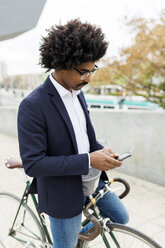 Spain, Barcelona, businessman on bicycle using cell phone in the city - VABF02258