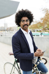 Spain, Barcelona, portrait of businessman with bicycle and cell phone in the city - VABF02259