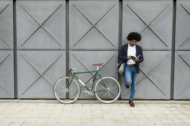 Businessman with bicycle leaning against a wall reading book - VABF02262