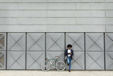 Geschäftsmann mit Fahrrad lehnt an einer Wand und liest ein Buch - VABF02263