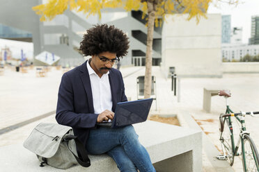 Spain, Barcelona, businessman with bicycle in the city sitting on bench using laptop - VABF02269