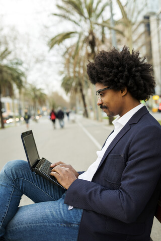 Spain, Barcelona, businessman in the city sitting on bench using laptop stock photo