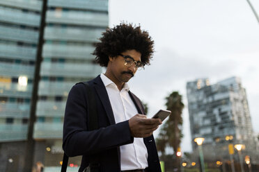 Spain, Barcelona, businessman in the city using cell phone at dusk - VABF02316