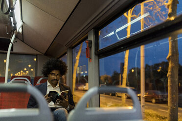 Spain, Barcelona, businessman in a tram at night reading a book - VABF02329