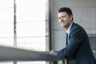 Smiling businessman leaning on railing - DIGF06408