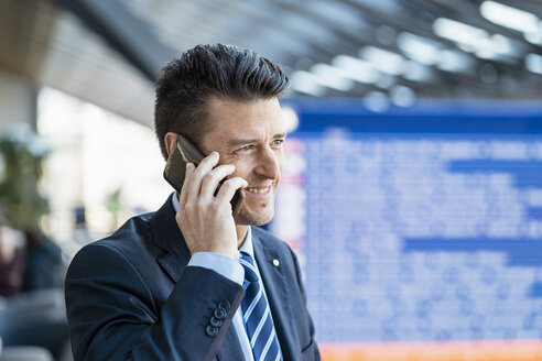 Lächelnder Geschäftsmann mit Handy am Bahnhof - DIGF06414