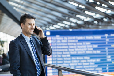 Lächelnder Geschäftsmann mit Handy am Bahnhof - DIGF06416