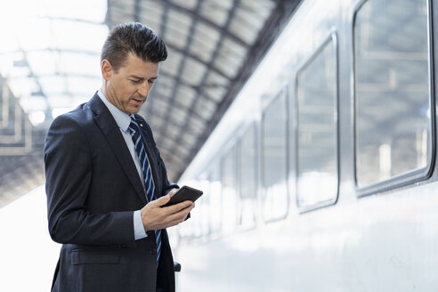 Geschäftsmann benutzt Mobiltelefon auf dem Bahnsteig - DIGF06421