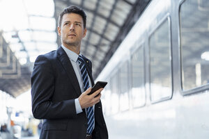 Geschäftsmann mit Mobiltelefon auf dem Bahnsteig - DIGF06422