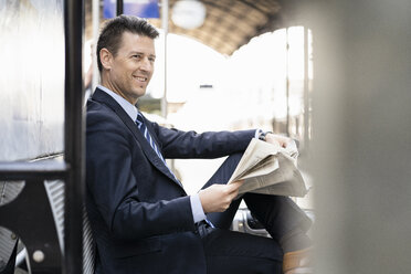 Lächelnder Geschäftsmann, der auf dem Bahnsteig Zeitung liest - DIGF06424