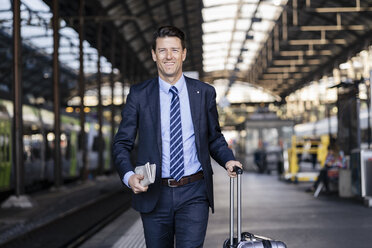 Lächelnder Geschäftsmann mit Koffer auf dem Bahnsteig - DIGF06428