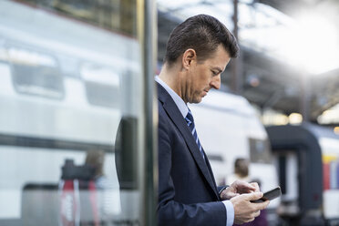 Geschäftsmann benutzt Mobiltelefon am Bahnhof - DIGF06429