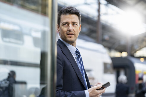 Geschäftsmann mit Mobiltelefon am Bahnhof - DIGF06430