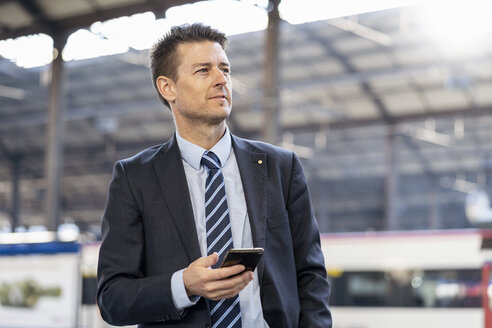 Geschäftsmann mit Mobiltelefon am Bahnhof - DIGF06435