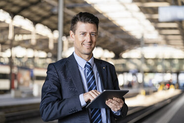 Porträt eines lächelnden Geschäftsmannes, der ein Tablet am Bahnhof benutzt - DIGF06441