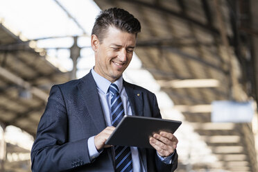 Smiling businessman using tablet at train station - DIGF06442