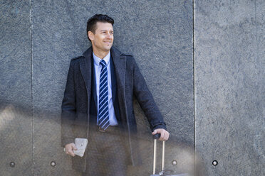 Lächelnder Geschäftsmann mit Koffer an einer Wand stehend - DIGF06457