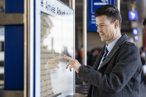 Geschäftsmann bei der Kontrolle der Abfahrtstafel am Bahnhof, lizenzfreies Stockfoto