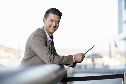 Lächelnder Geschäftsmann mit Tablet stehend im Freien, lizenzfreies Stockfoto